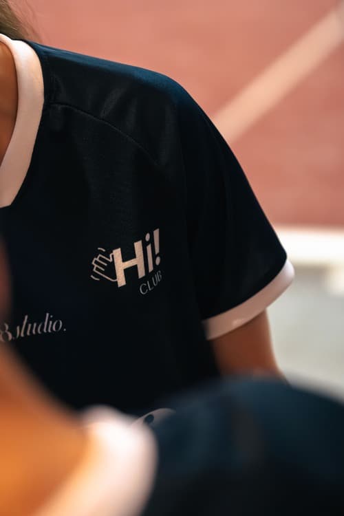 A Hi! Club jersey β navy with blush trim, crest on the chest β worn courtside.